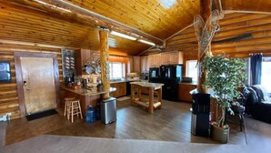 A spacious log cabin interior with a kitchen, dining area, and a large window. - 2010 Steese Hwy · Aurora viewing, quiet space, entire log home (Fairbanks)