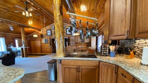 A spacious kitchen with wooden cabinets, granite countertops, and hanging pots. - 2010 Steese Hwy · Aurora viewing, quiet space, entire log home (Fairbanks)