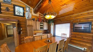 A wooden interior with a dining table and chairs, framed pictures on the walls, and a ceiling light fixture. - 2010 Steese Hwy · Aurora viewing, quiet space, entire log home (Fairbanks)