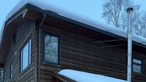 A two-story wooden cabin with a garage, a covered porch, and a snow-covered roof. - R & R Hideaway Suite (Fairbanks)
