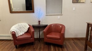 A room with two red leather chairs, a small table with a decorative item, a mirror, and a window with blinds. - R & R Hideaway Suite (Fairbanks)