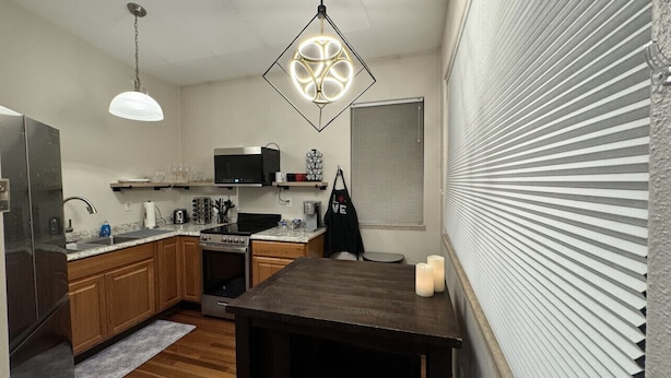 A compact kitchen with wooden cabinets, a microwave, a stove, and a hanging light fixture. - R & R Hideaway Suite (Fairbanks)