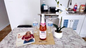Una encimera de cocina con una revista, una botella de Welch's Sparkling Raspberry, botellas de agua y una orquídea en maceta.