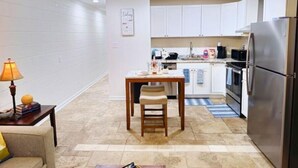 Una cocina compacta con gabinetes blancos, una mesa de comedor con sillas, un refrigerador y un ventilador de techo.