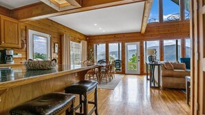 A spacious kitchen with wooden cabinets, a dining area with chairs, and a large window offering a view of the mountains. - Dream Catcher Mountain View Cabin (Pigeon Forge)