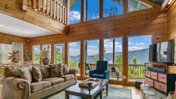 A spacious living room with a large wooden ceiling, a sofa, a coffee table, and a TV on a wooden cabinet. - Dream Catcher Mountain View Cabin (Pigeon Forge)