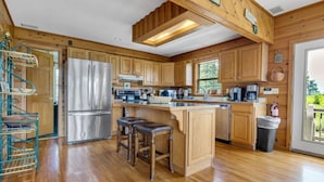 A spacious kitchen with wooden cabinets, a stainless steel refrigerator, and a large island with stools. - Dream Catcher Mountain View Cabin (Pigeon Forge)