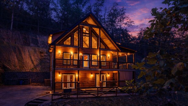 A two-story log cabin with a balcony, surrounded by trees and a rocky hillside. - Ultimate Smoky Getaway: Hot Tub, Fun & Fresh Air in the Heart of the Smokies. (Sevierville)