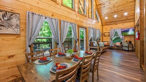 A wooden cabin with a dining area set for four, featuring a long table, wooden chairs, and a view of the outdoors. - Ultimate Smoky Getaway: Hot Tub, Fun & Fresh Air in the Heart of the Smokies. (Sevierville)