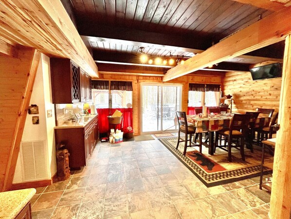 A cozy log cabin interior with a dining area, kitchen, and a large sliding glass door leading to an outdoor patio.