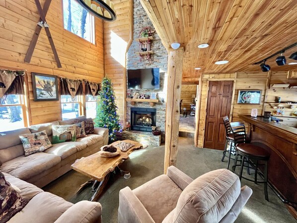 A cozy cabin interior with a fireplace, wooden walls, a sofa, and a Christmas tree. - Winter Season Rental - Ski in/out, Hot Tub, Fire Pit (Somerset)