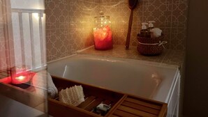 A bathroom with a bathtub, a wooden brush, a candle, and a basket with toiletries. - Le Bijou du Minage - Jardin/terrasse - Hypercentre LA Rochelle (La Rochelle)