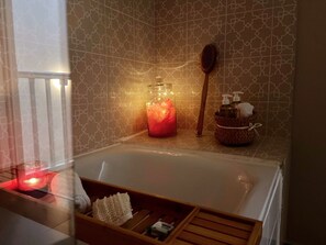 Ein Badezimmer mit einer Badewanne, einer Holzbürste, einer Kerze und einem Korb mit Pflegeprodukten.