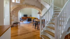 Amplia sala de estar con piso de madera, una mesa de comedor y una escalera con barandales blancos.