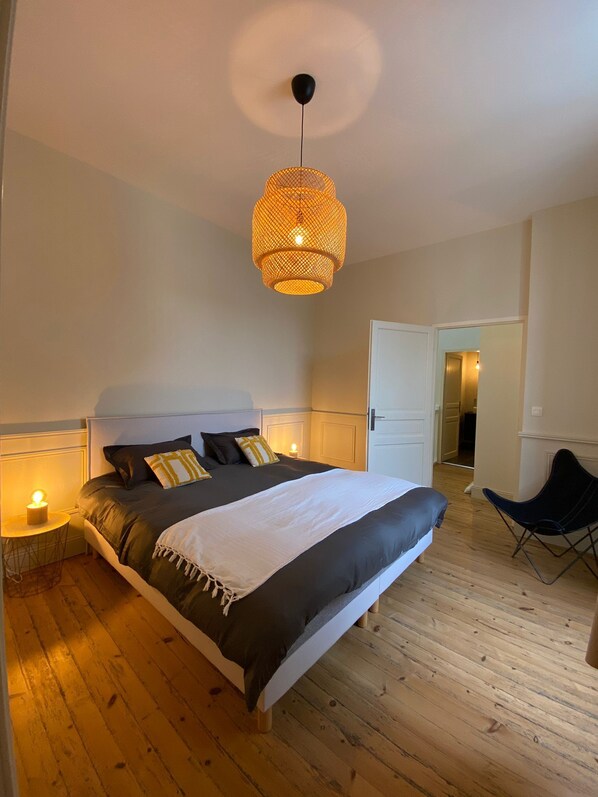 Ein Schlafzimmer mit einem Bett, Nachttischlampen, einer Pendelleuchte und einem Sessel.