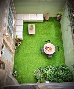 A rooftop garden with a dining table and chairs, a sofa, and potted plants.