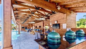 Un espacio al aire libre cubierto con piscina, asientos de madera y parrillas de barbacoa.