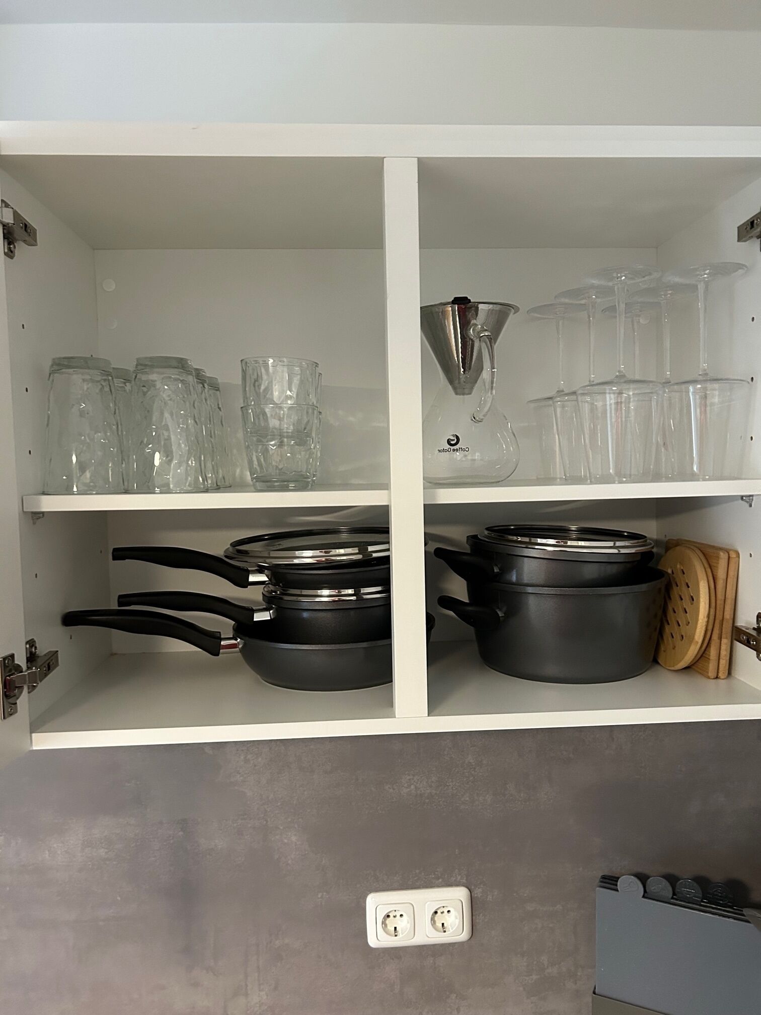 Une cuisine avec des meubles blancs, de la vaisselle en verre et des ustensiles de cuisine noirs.