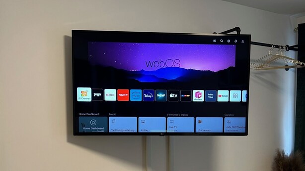 Un televisor de pantalla plana montado en la pared, mostrando una pantalla de inicio con distintos servicios de transmisión.