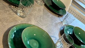 Una mesa servida con platos verdes, tazones y vasos transparentes.