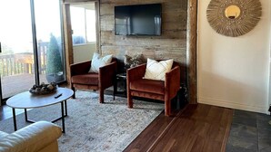 A living room with a wooden wall panel, a flat-screen TV, two leather armchairs, a coffee table, and a decorative wall piece.