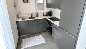 Eine kleine Küche mit grauen Schränken, einem Edelstahlkühlschrank, einem eingebauten Backofen und einem Fenster mit Milchglasverblendung.
