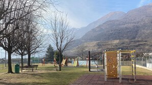 Ein Park mit Spielgeräten, Bänken und Blick auf die Berge.
