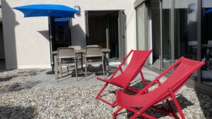 Eine Terrasse mit Sitzmöglichkeiten im Freien, darunter zwei rote Liegestühle und ein Tisch mit Stühlen, unter einem blauen Sonnenschirm.