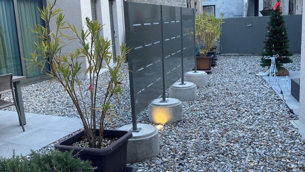 Ein Innenhof mit Kiesboden, Blumentöpfen, einem Metallzaun und einer kleinen Weihnachtstanne.