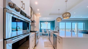 A modern kitchen with a large island, stainless steel appliances, and pendant lighting. - Beach One: Style Meets the Shore w/ Pool and Spa (Treasure Island)