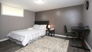 A bedroom with a bed, bedside table, chair, desk, and a small rug.