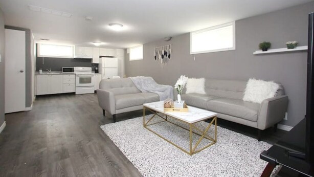 A modern apartment with a kitchen, two grey sofas, a coffee table, and a TV.