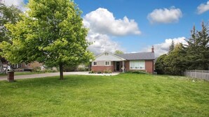 A single-story house with a front lawn, a driveway, and a tree.