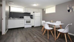 A modern kitchen with white cabinets, a microwave, oven, and refrigerator. There is a dining table with four chairs.