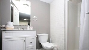 A bathroom with a white vanity, a toilet, and a shower area.