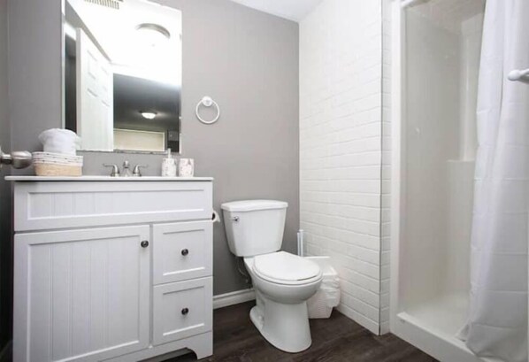 A bathroom with a white vanity, a toilet, and a shower area.