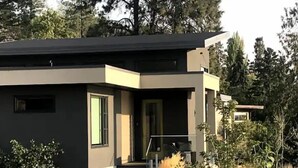 Ett modernt hus i två våningar med en mörk fasad, en ytterdörr och en liten veranda med trappsteg som leder upp till den.