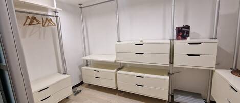 A walk-in closet with multiple drawers and shelves, a hanging rod, and a small shelf with a box and a bottle.