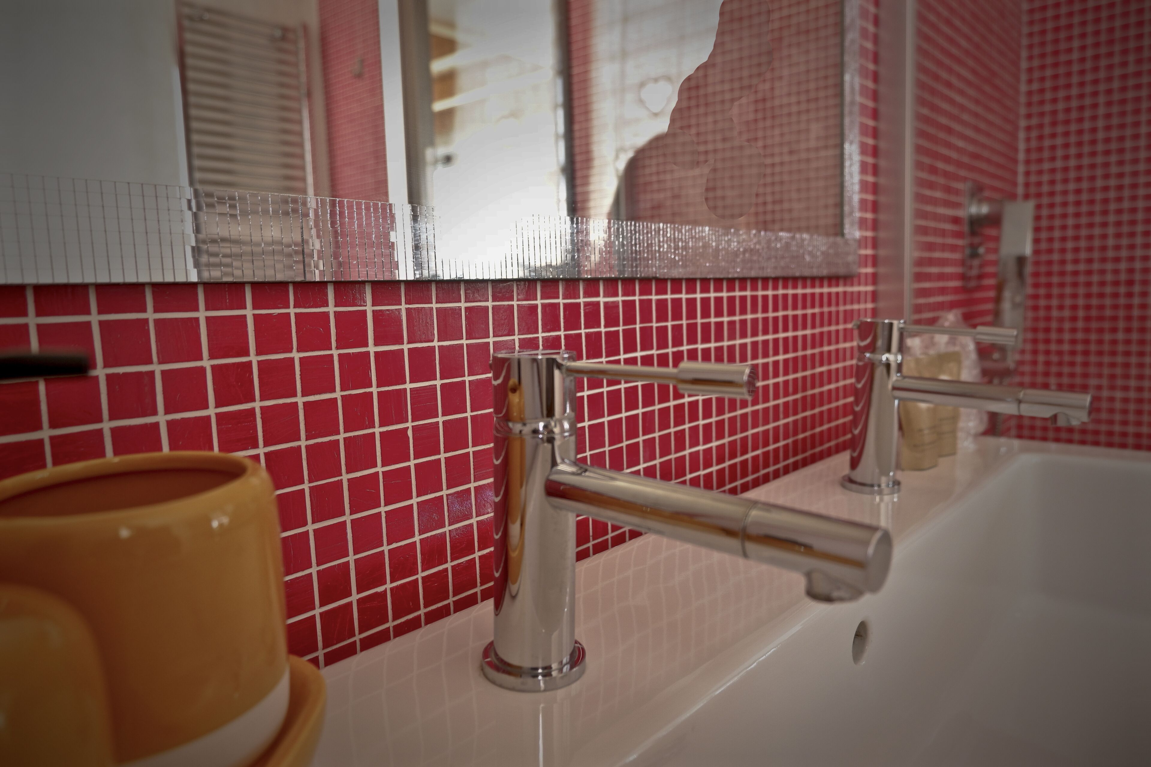 A bathroom with a white sink, chrome faucet, and red tiled walls.