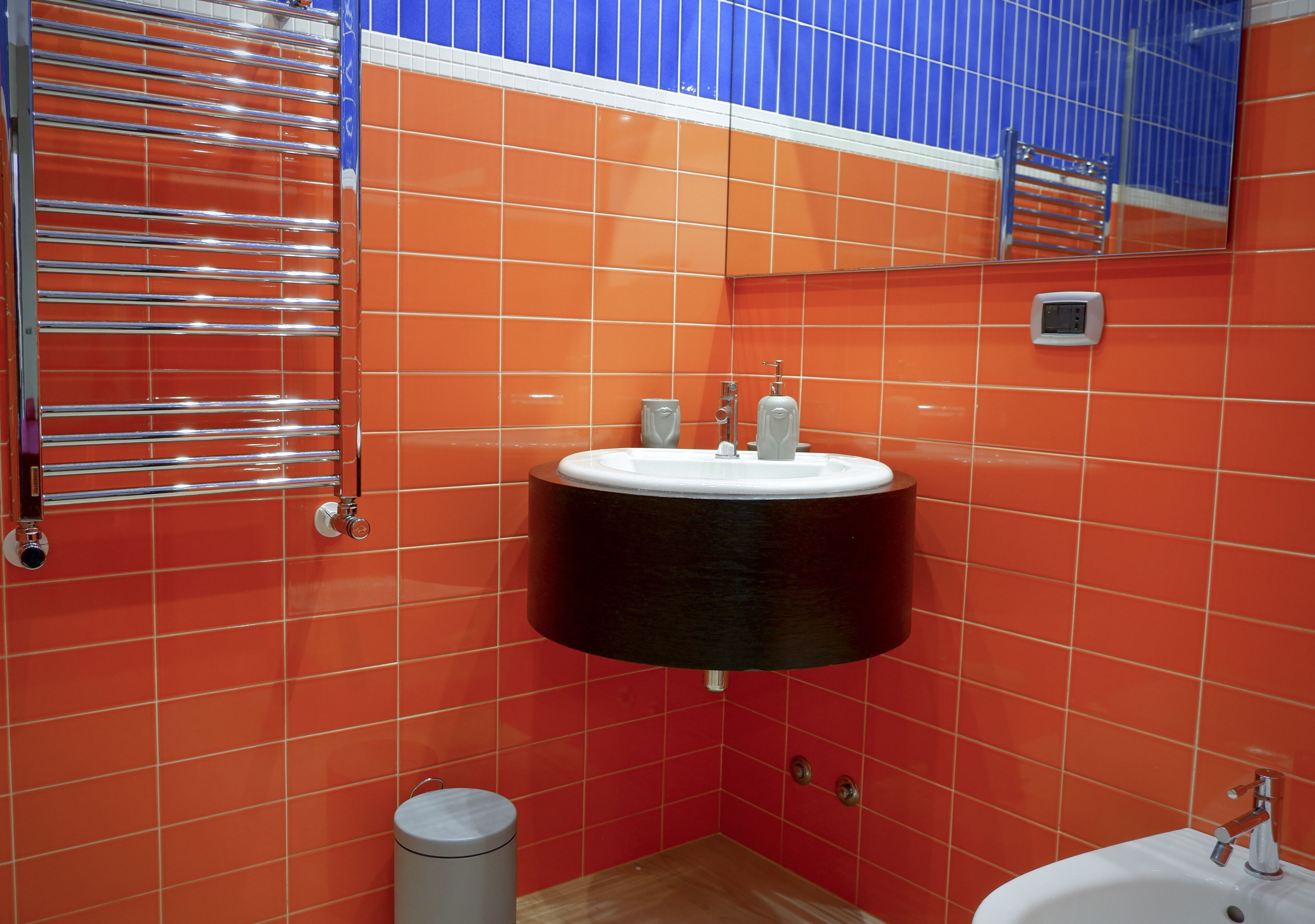 Une salle de bain avec des murs recouverts de carreaux orange, un lavabo noir, des toilettes blanches et un miroir au-dessus du lavabo.