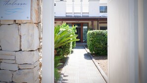 A stone wall with a sign, a paved pathway, and a building entrance with a door and windows. - Thalassa Bari (Bari)