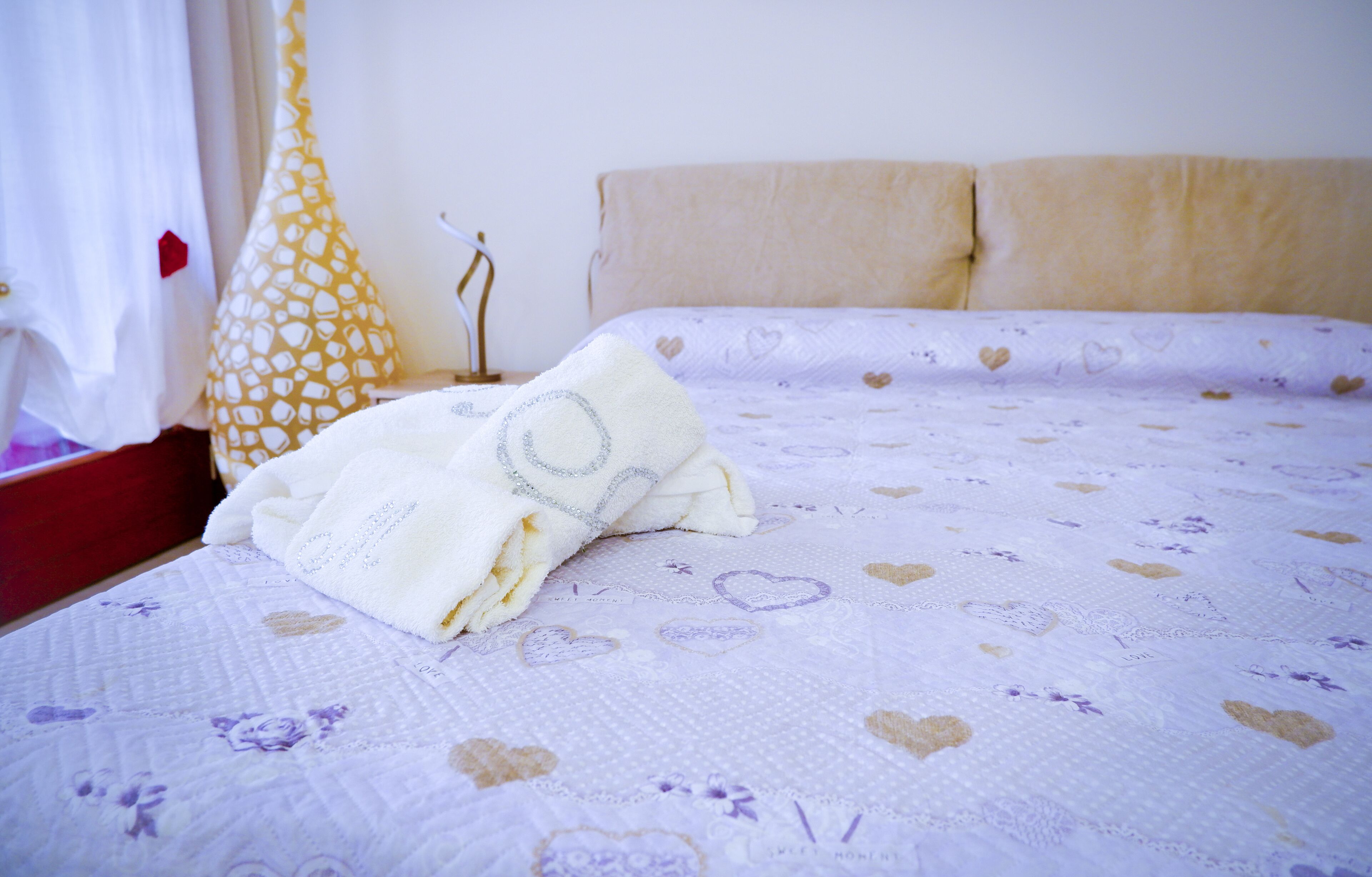 A bed with a white and purple floral bedspread, a white pillow, and a yellow decorative pillow.