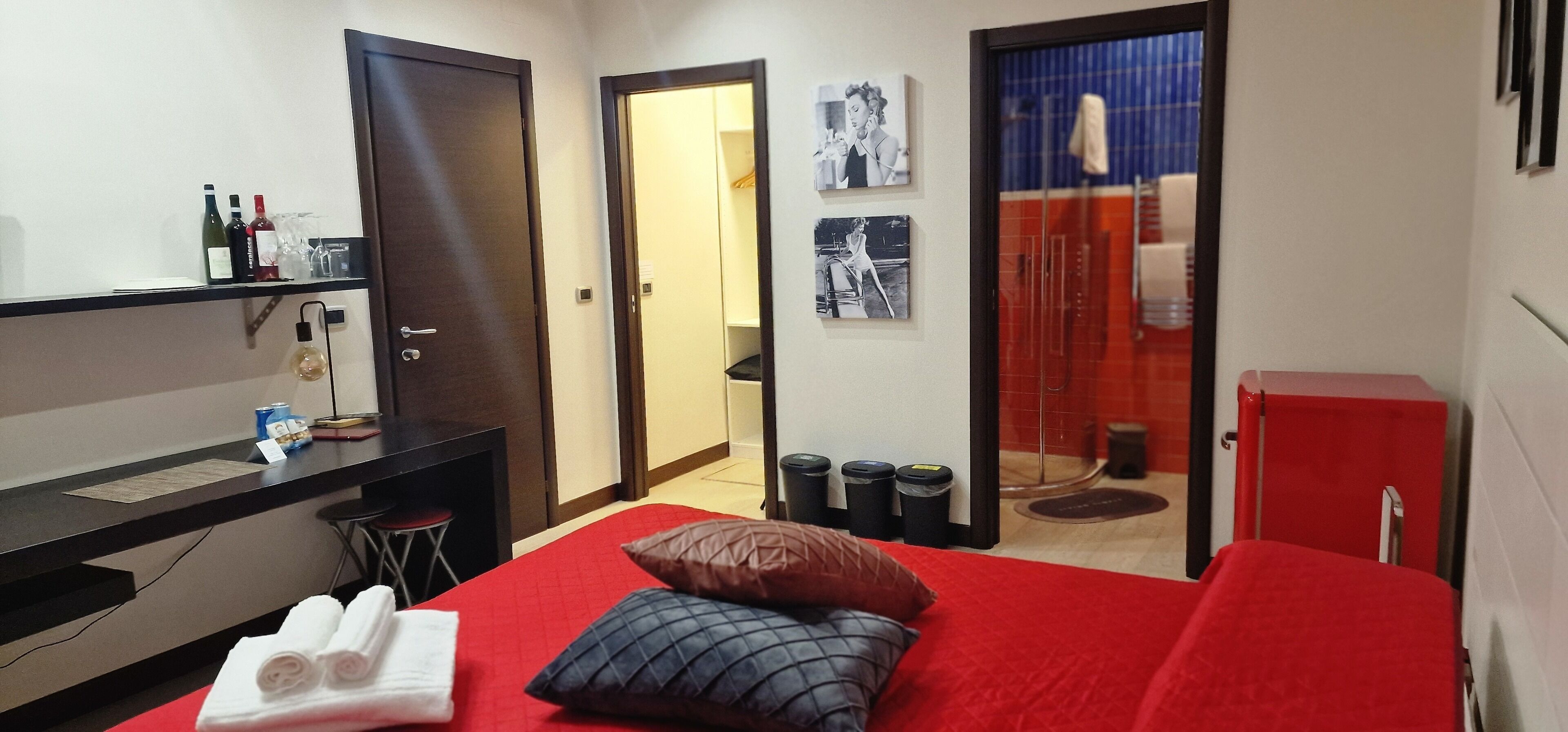 Quarto de hotel com cama, escrivaninha, cadeira, sofá vermelho, armário vermelho, espelho e porta para o banheiro.