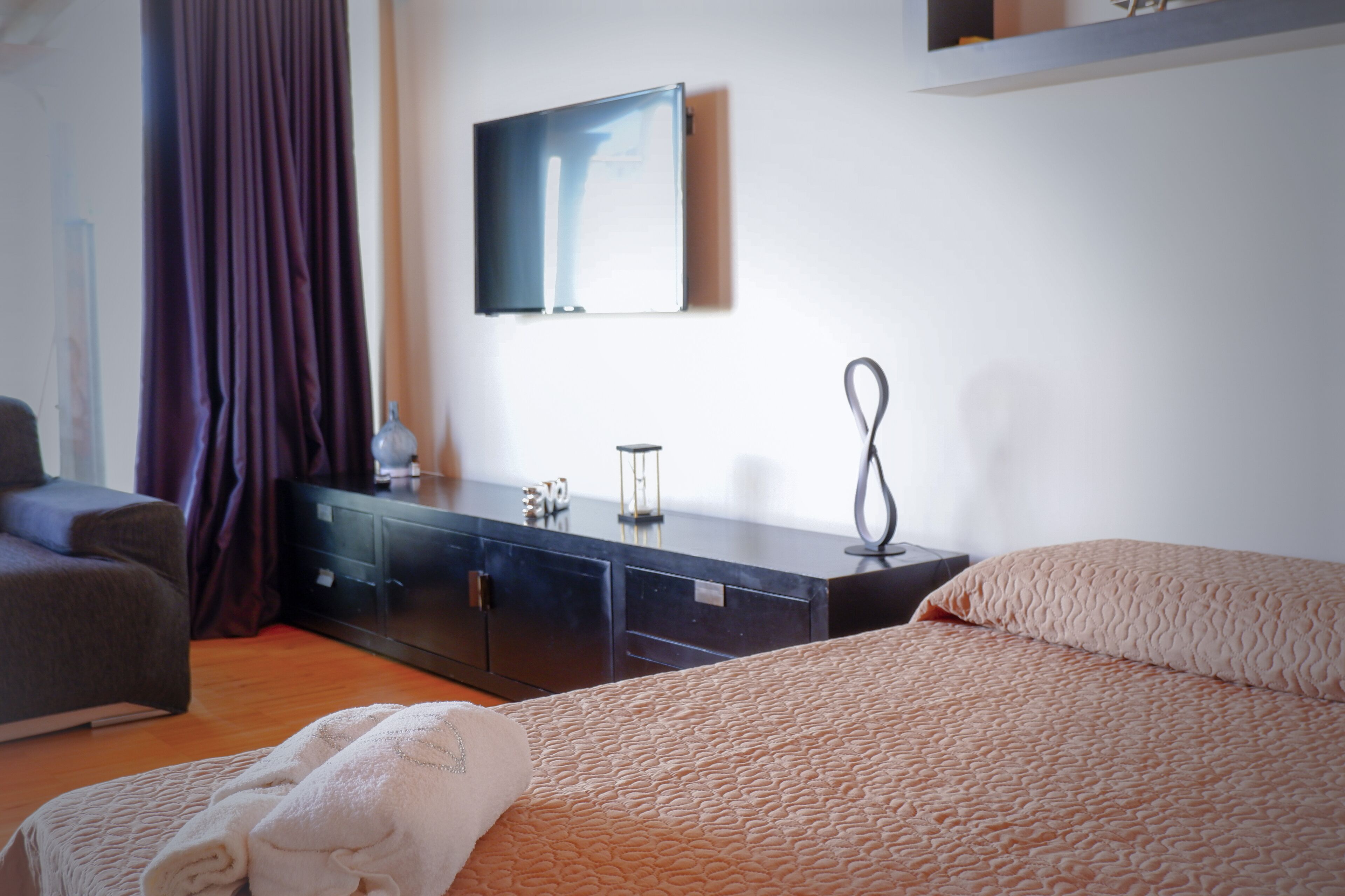 A bedroom with a bed, a dresser, a television on the wall, and a window with curtains.
