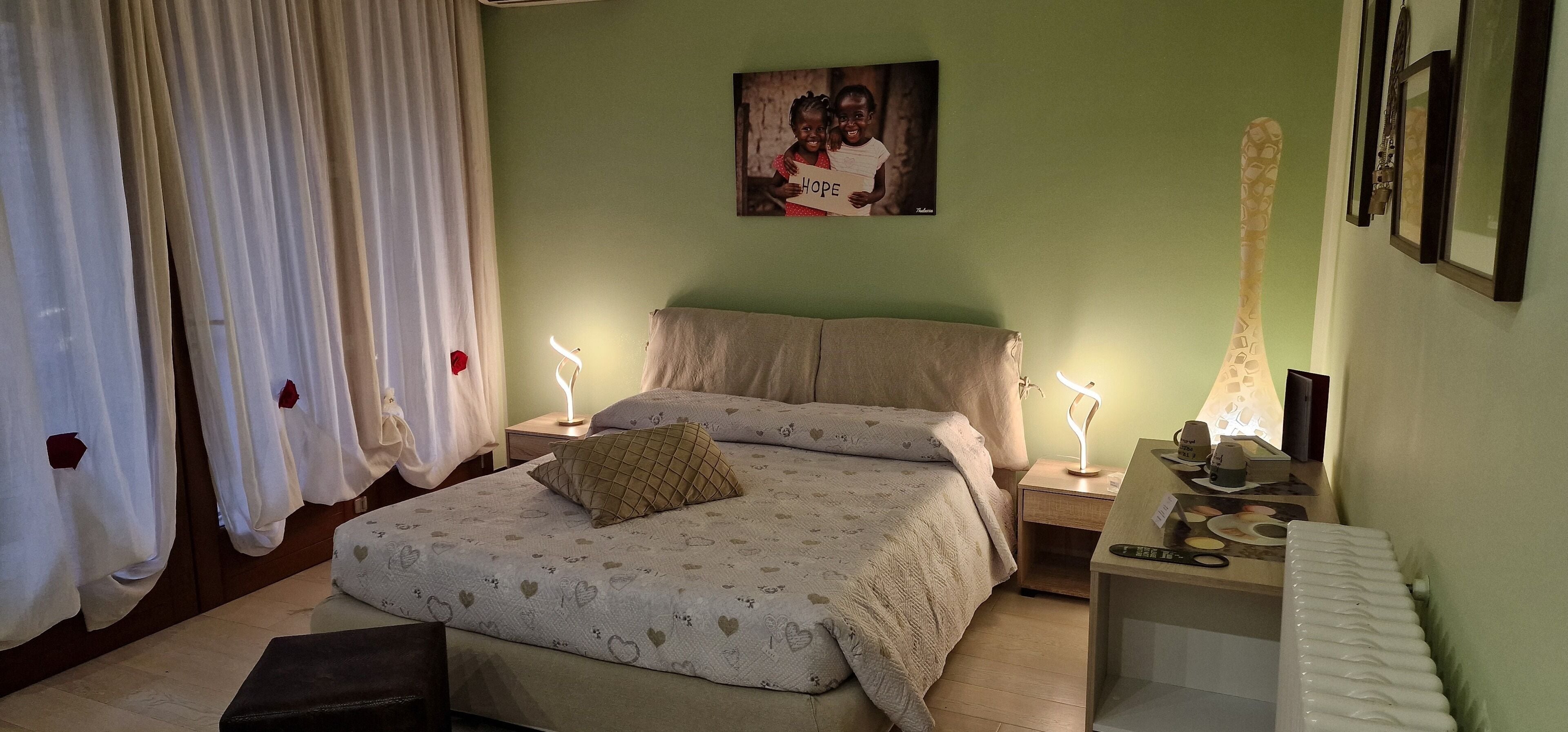 A bedroom with a bed, bedside tables, a nightstand, a lamp, a radiator, and a painting on the wall.