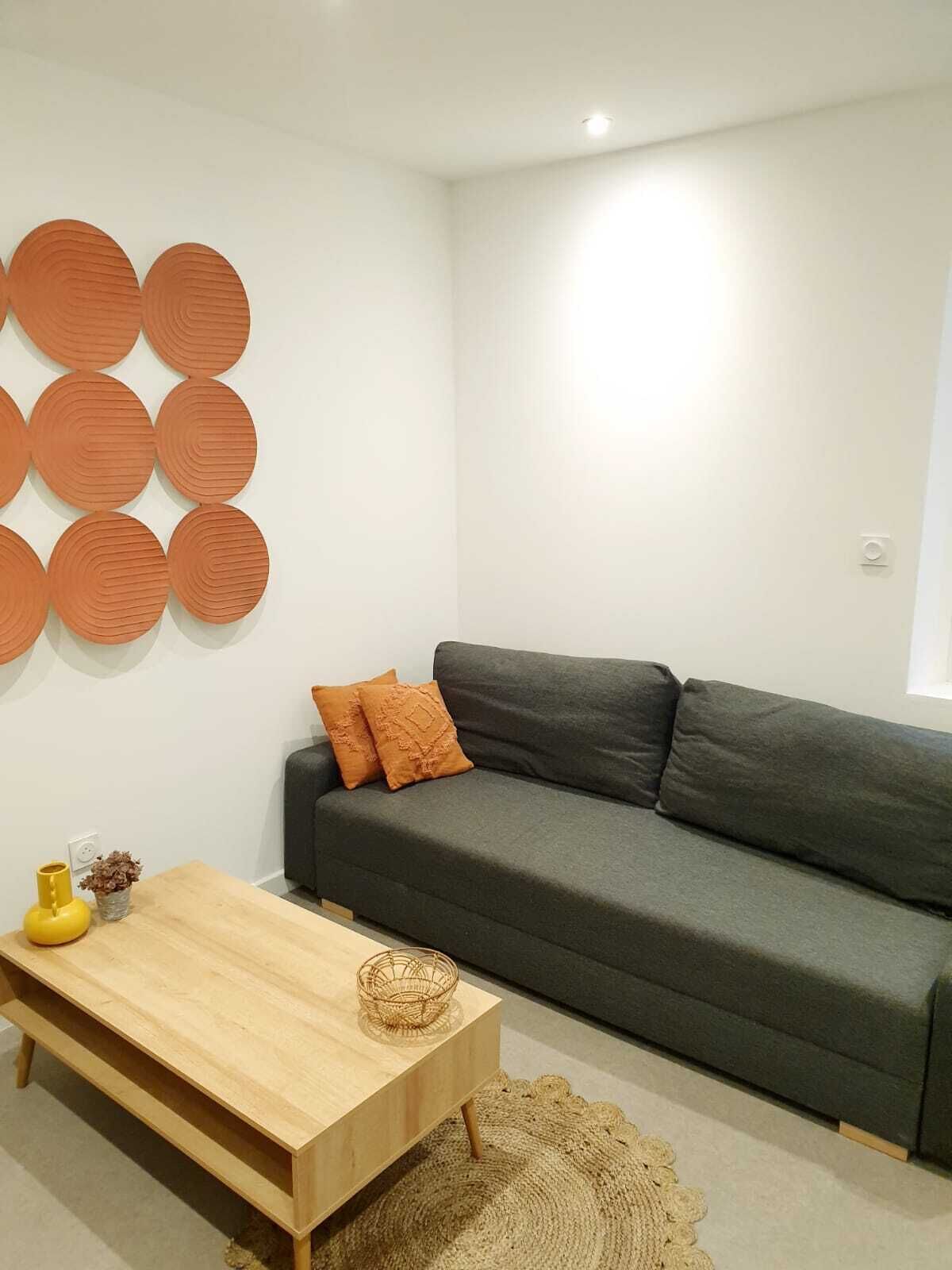 Una sala de estar con un sofá gris, una mesa de centro de madera y un adorno circular en la pared.