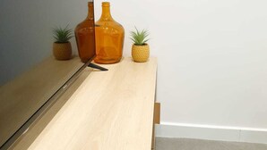 A wooden TV stand with a flat-screen TV, two orange glass bottles, and two small potted plants. - The bohemian (Pamiers)