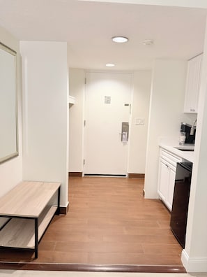 A hallway with a bench, a door, and a kitchen area with cabinets and a dishwasher. - The Boston Hotel  (Boston)