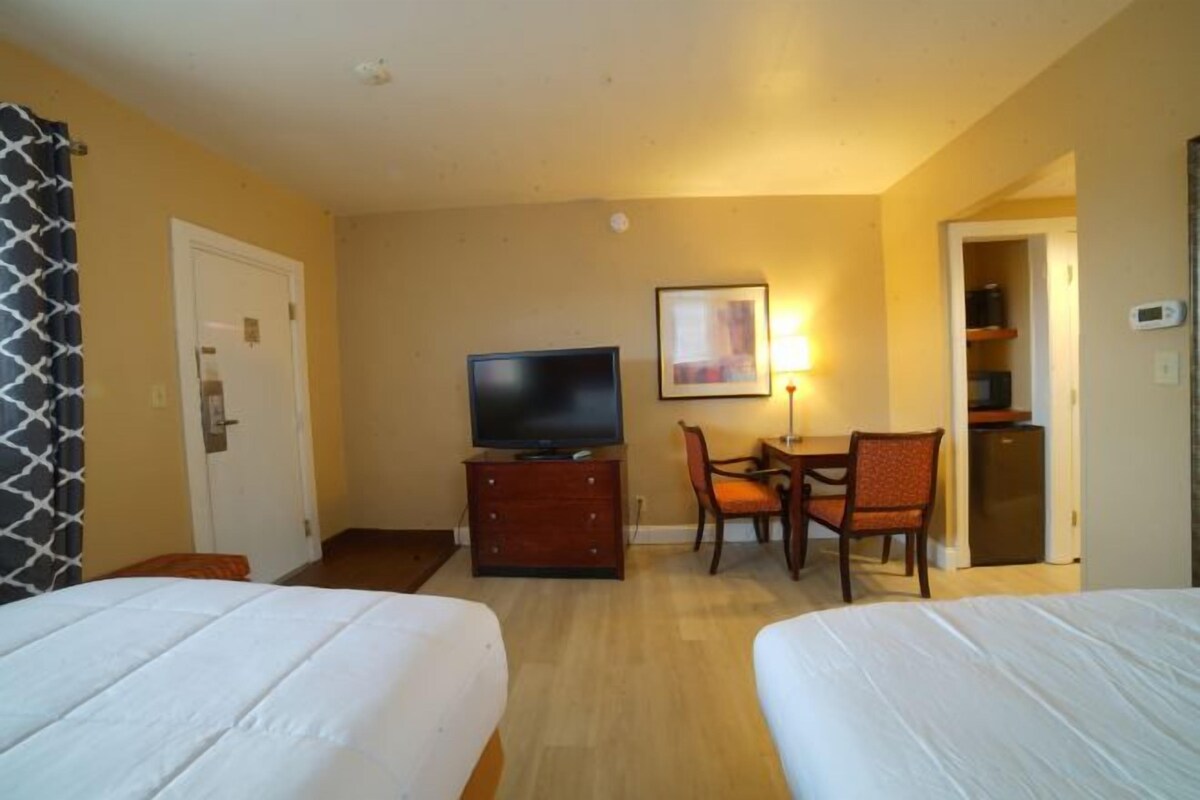 A hotel room with two beds, a TV on a wooden cabinet, a desk with a chair, and a dining area.