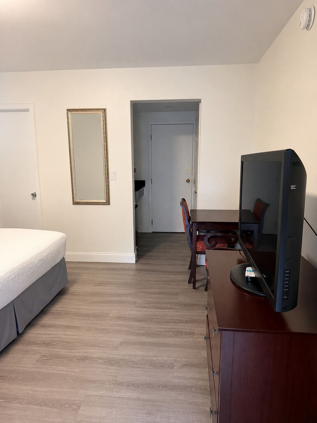 A hotel room with a bed, a desk with a computer, a chair, and a door leading to another room.
